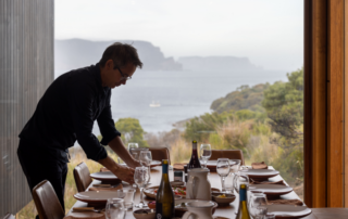 A server adjusts place settings at an elegantly prepared dining table overlooking a scenic coastal