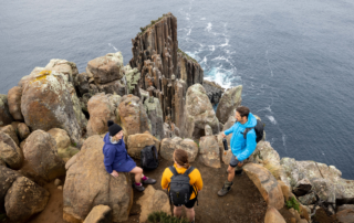 Three hikers in colorful jackets navigate dramatic rocky outcrops and columnar basalt formations
