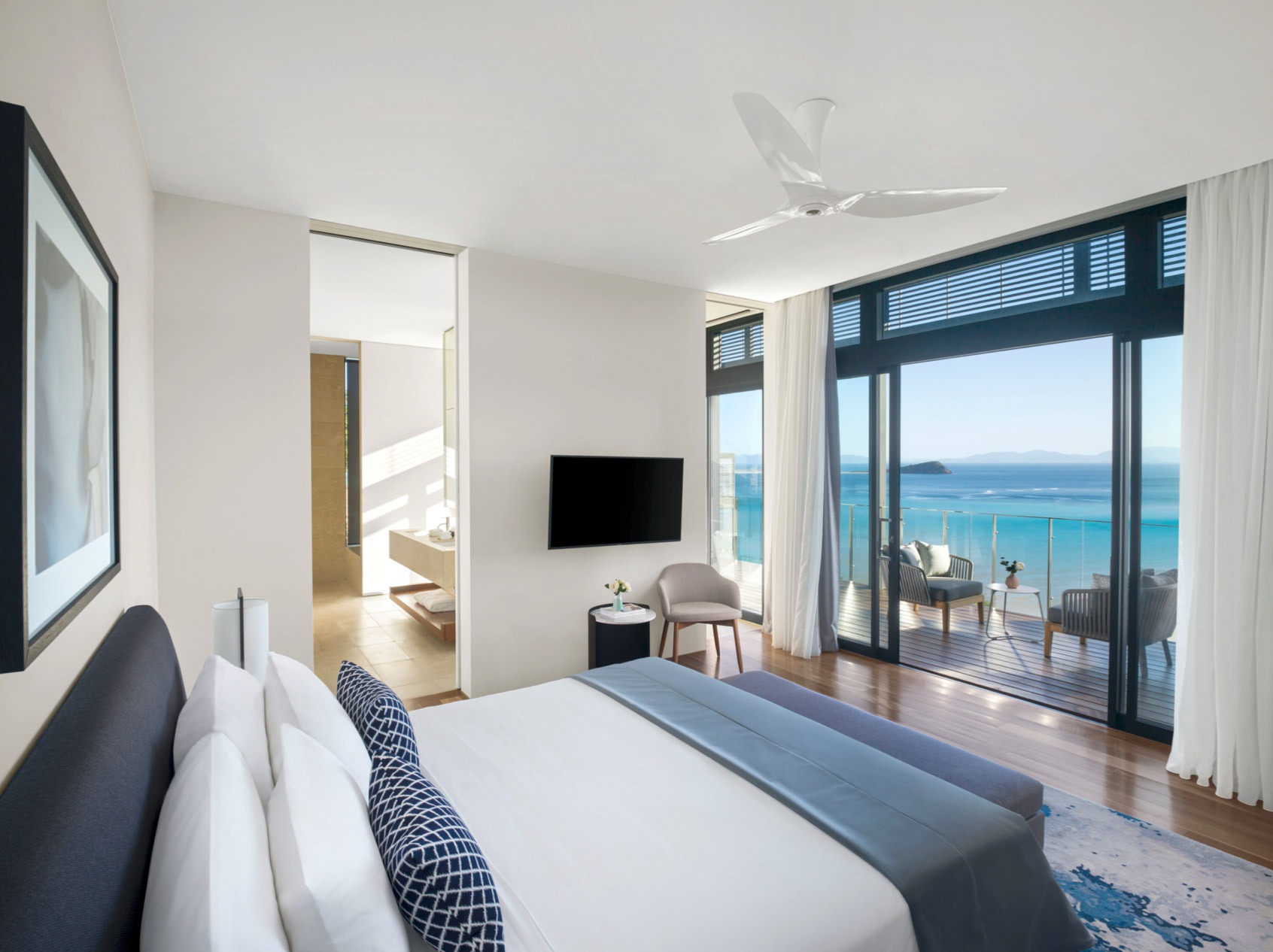 A contemporary luxury hotel suite featuring a king bed with ocean views through floor-to-ceiling