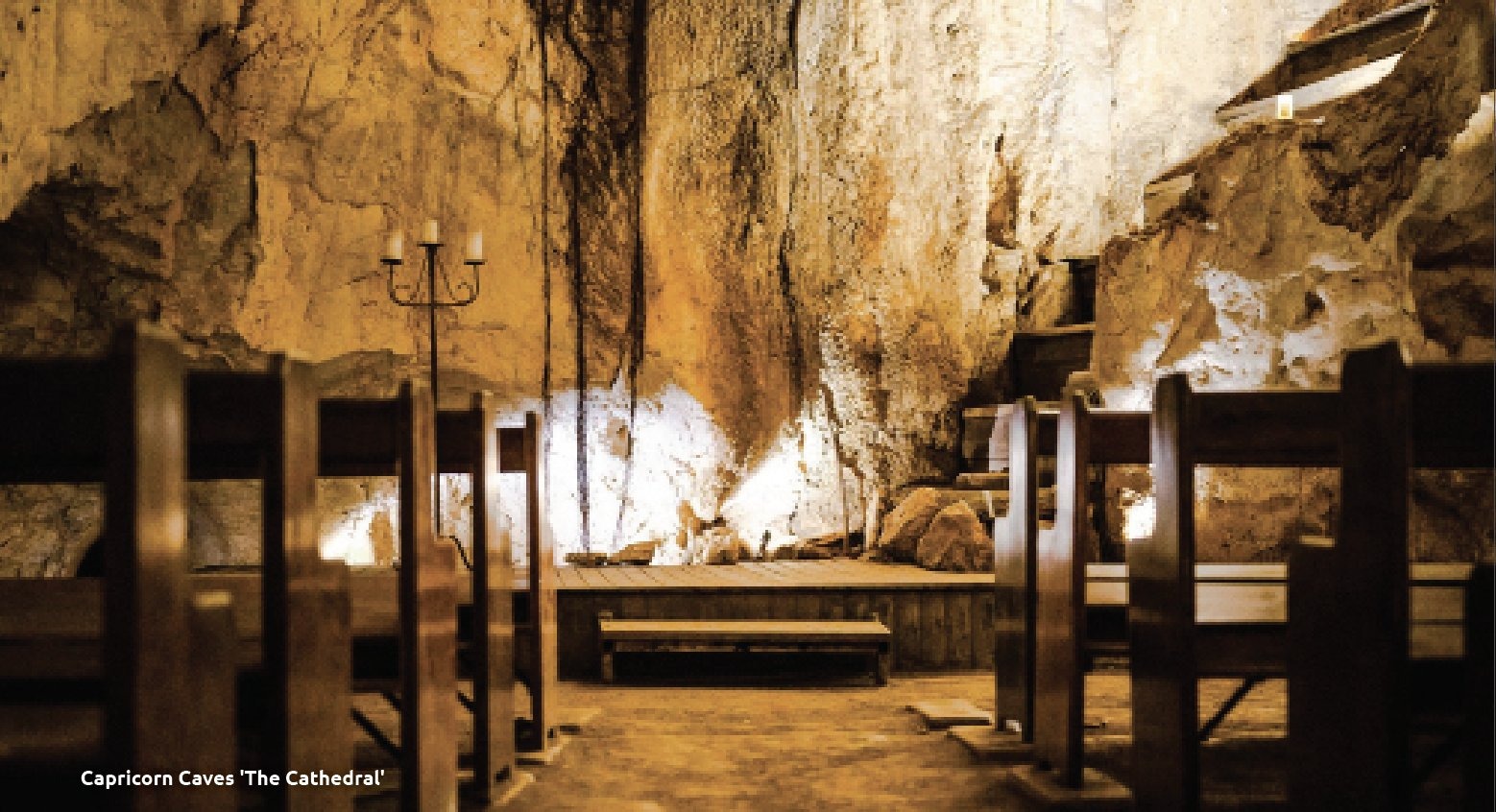 A historic underground cave chamber with wooden pews and candelabra, carved into ancient limestone