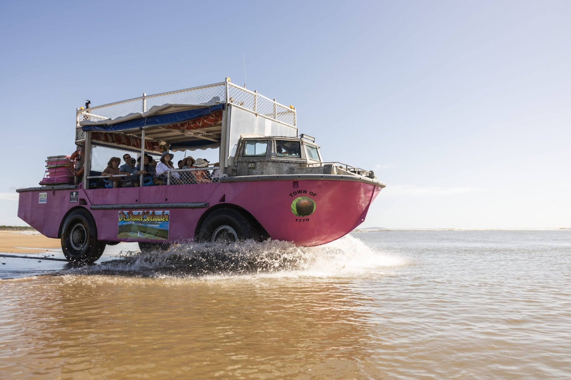 A bright magenta amphibious tour vehicle labeled '1770' and 'Town of...' carries tourists through