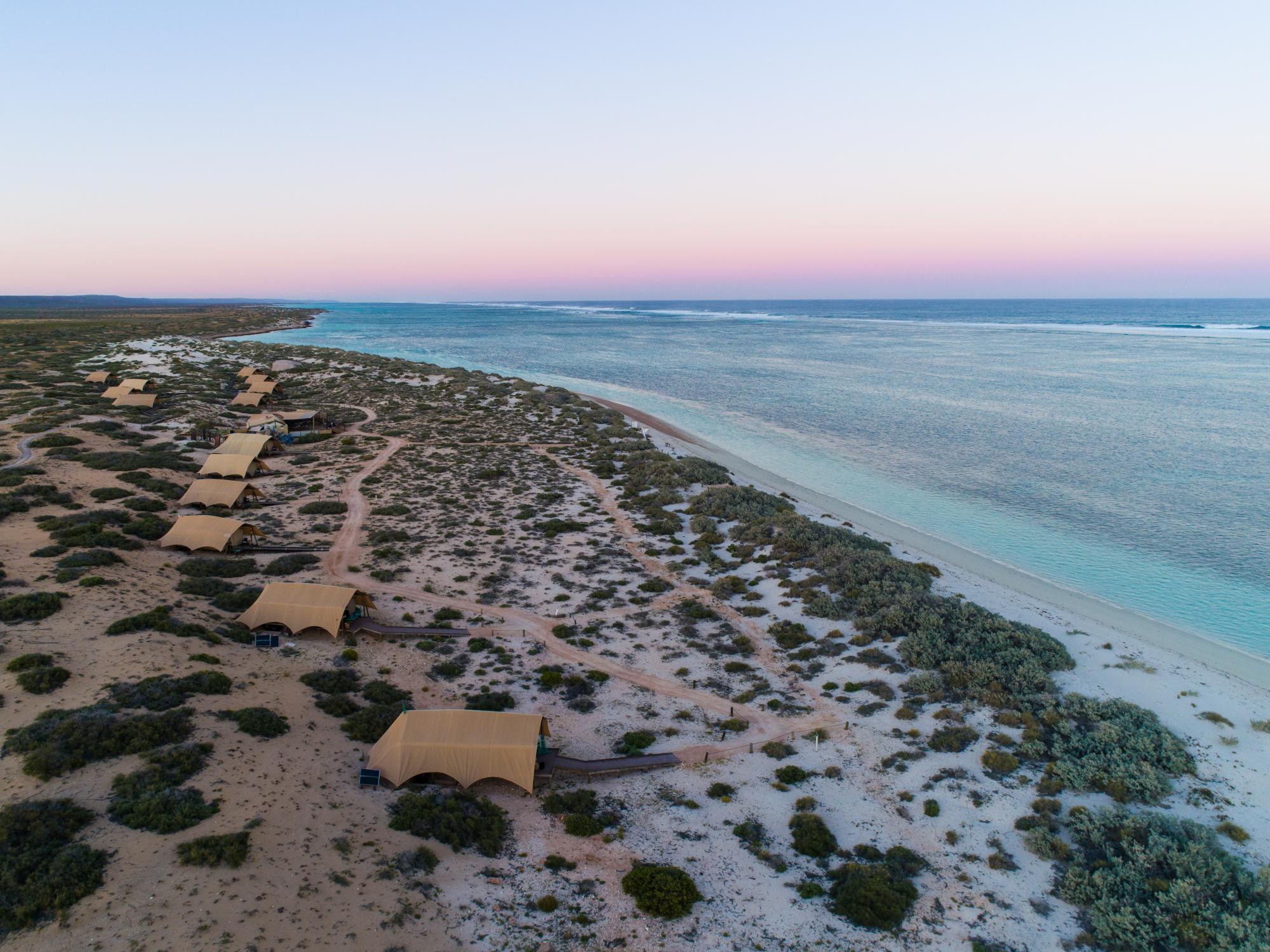 An aerial sunset view of an exclusive beachfront glamping resort with distinctive tan canvas