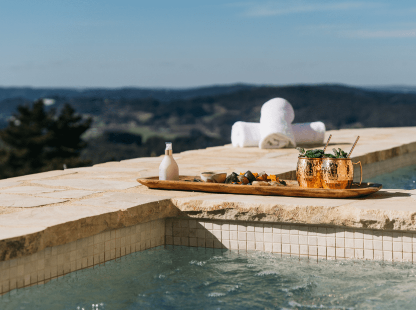 An elegant infinity pool with pristine waters and white tile trim overlooks a sprawling forested