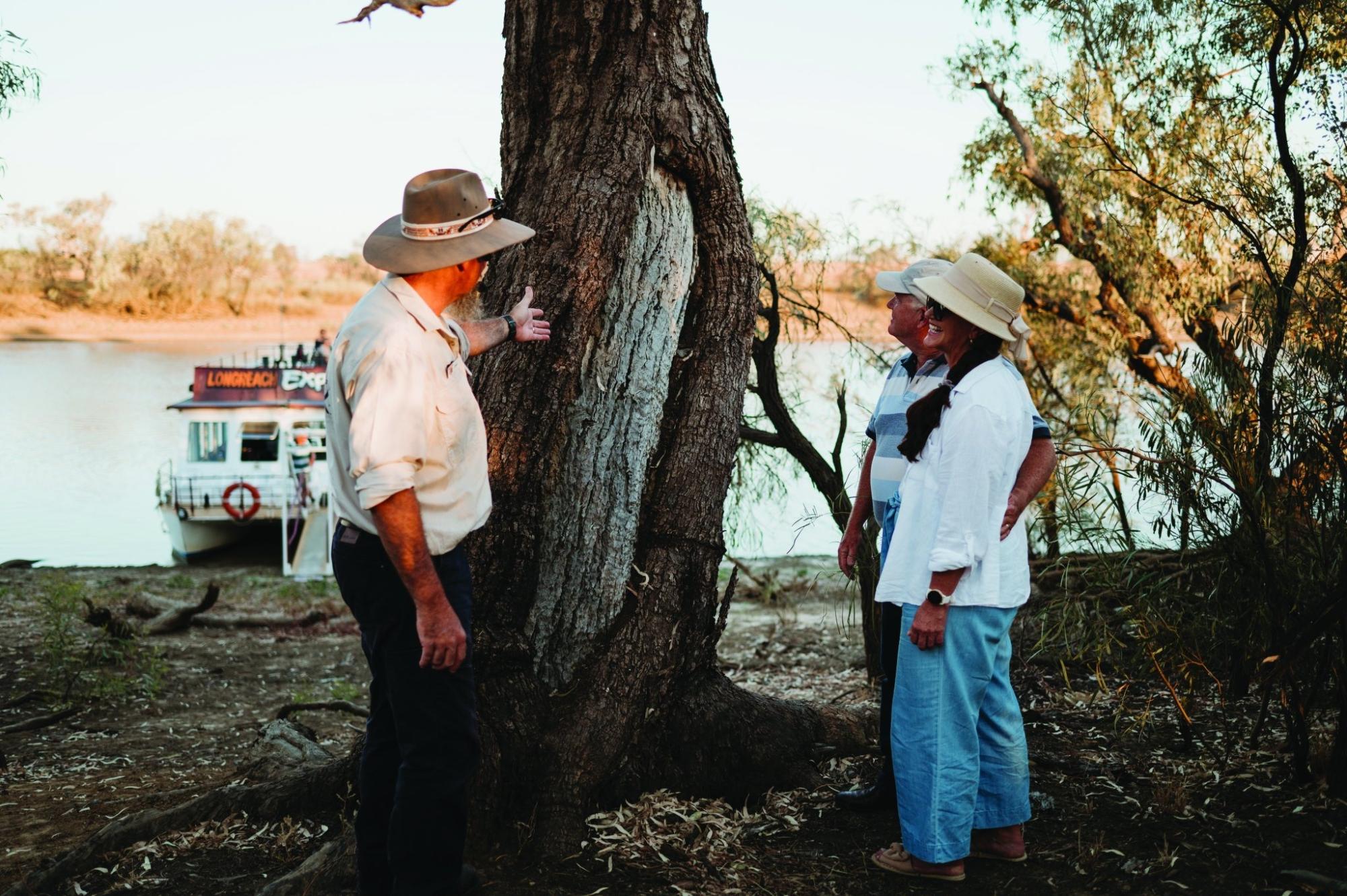 A uniformed riverboat captain and local guide examine a massive ancient tree on the riverbank